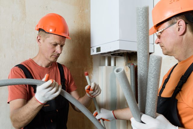 Workers are installing thermal insulation on the pipes of a home gas boiler.